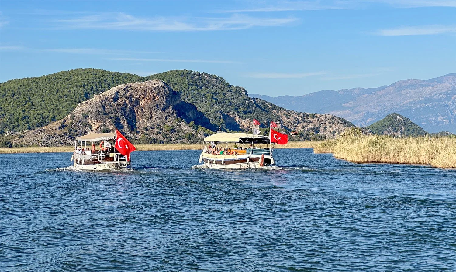 Two public ferries sailing on a wide river between Dalyan and Iztuzu Beach in Türkiye.