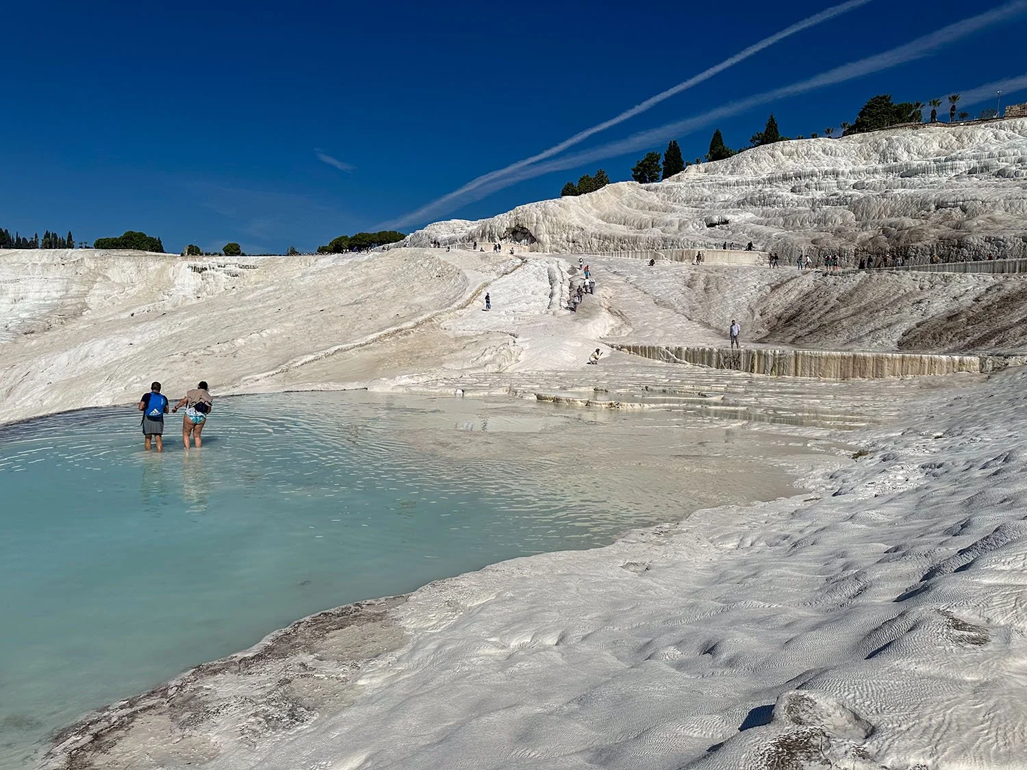 wide view of part of the Pamukkale travertine terraces with two tourists in the middle distance wading in one of the pools.