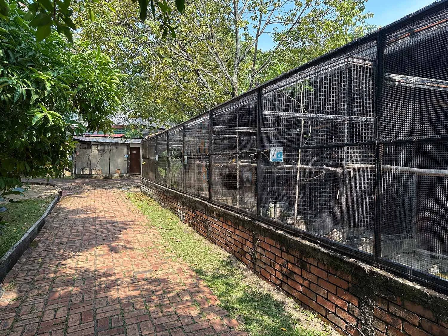 Large bird cages along a brick pathway at the Penang Bird Park in Butterworth, Malaysia.
