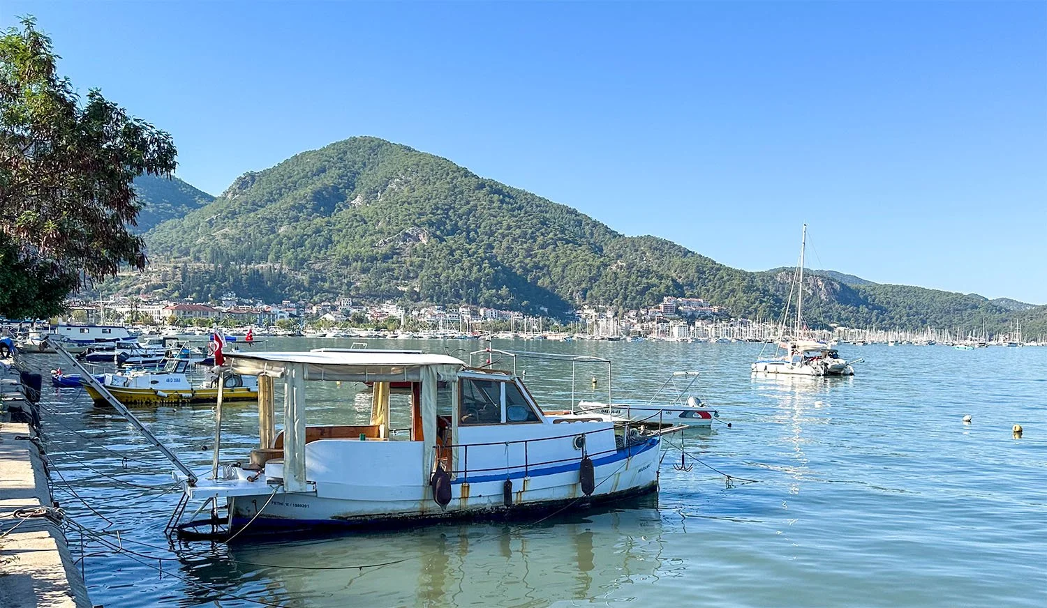 View along the waterfront at Fethiye on the Turkish Riviera with a small fishing boat in the foreground and many sailing yachts in the distance.