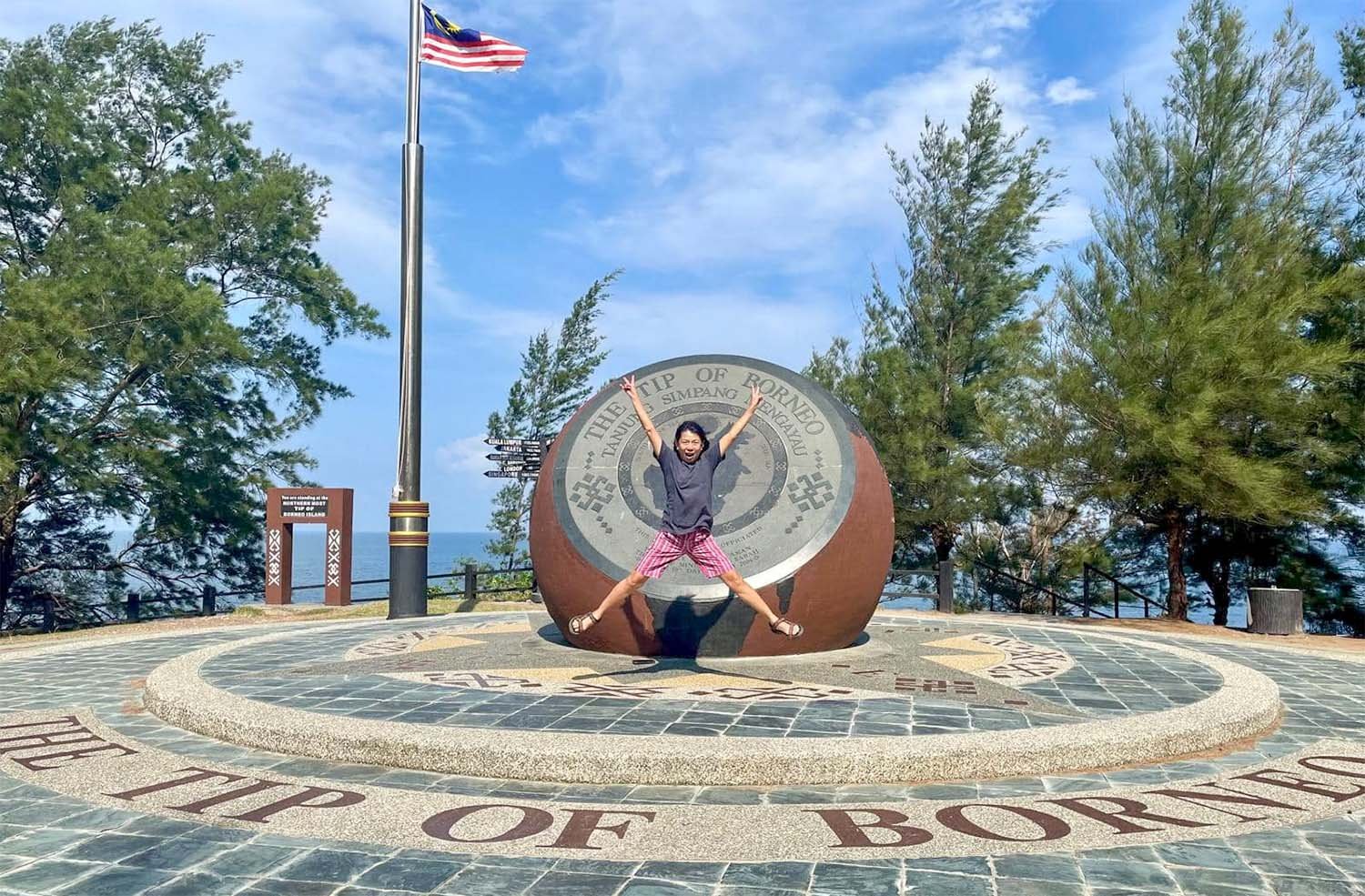 Woman making a star-shape jump in front of a monument at the Tip of Borneo, Malaysia.