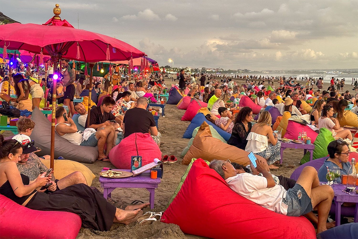 Hundreds of tourists sitting on colourful bean bags crowd a beach in southern Bali