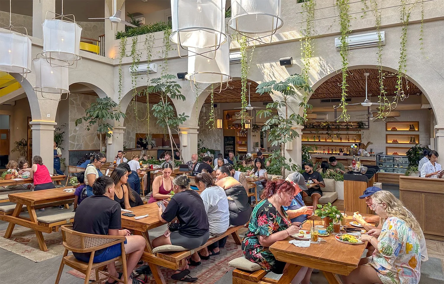 Interior view of the picturesque Milk & Madu cafe at Seminyak, Bali, with dozens of tourists eating breakfast or brunch.