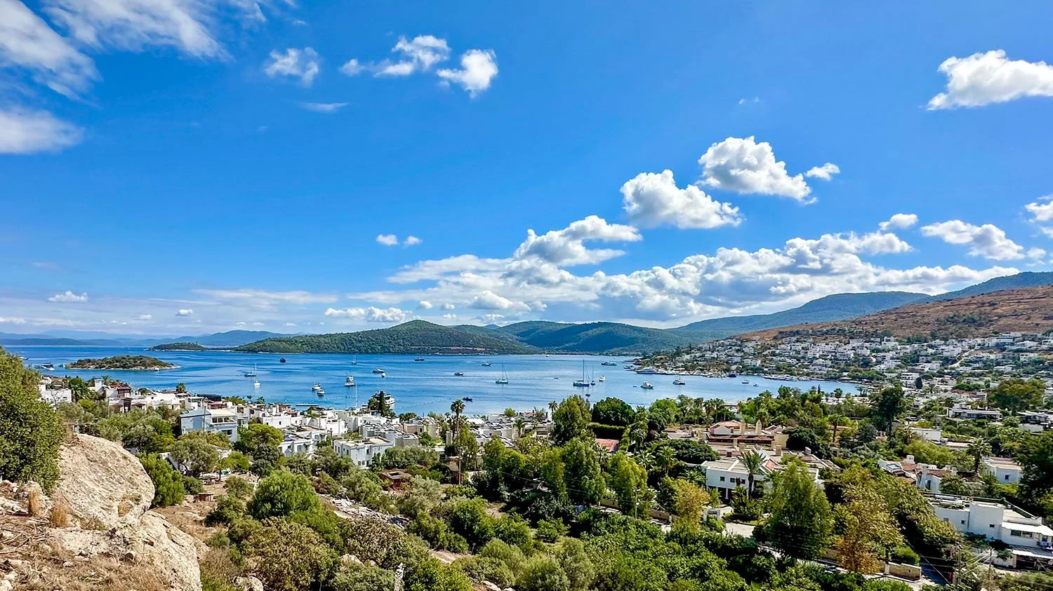 View Scenic coastal view across a wide bay under a sunny sky at Türkbükü near Gündoğan, Bodrum, Türkiye.