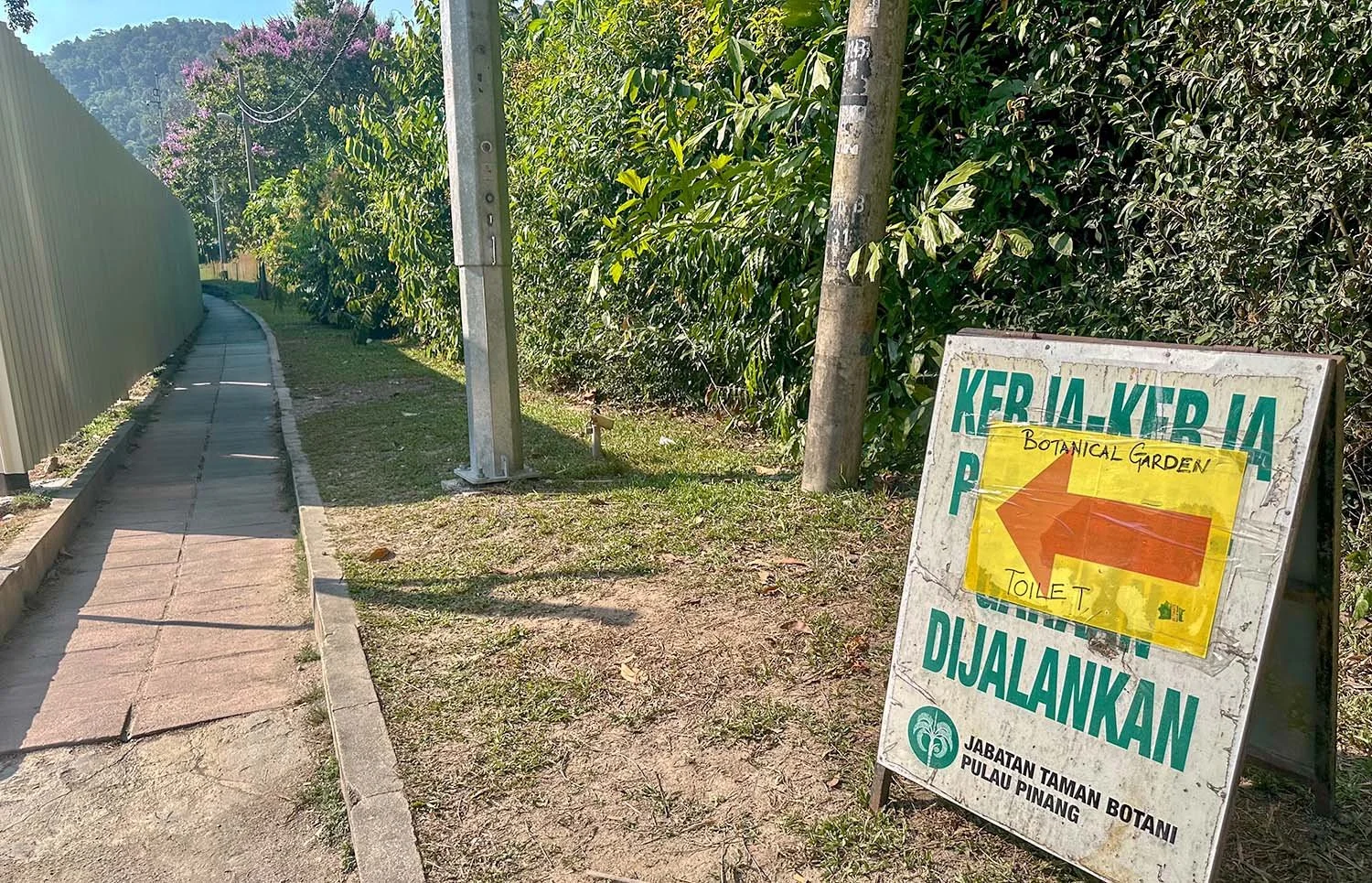 A dirty sign pointing to a temporary entrance pathway to the botanic gardens on Penang Island, Malaysia.