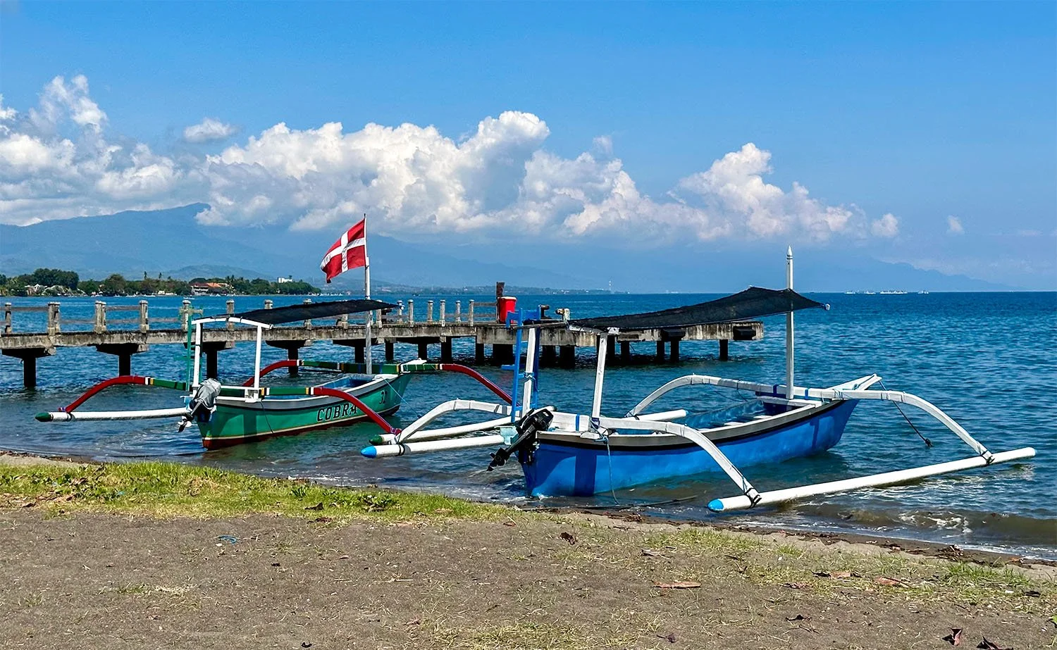Two dolphin-watching boats moored at Lovina Beach in North Bali with a small pier in the background.