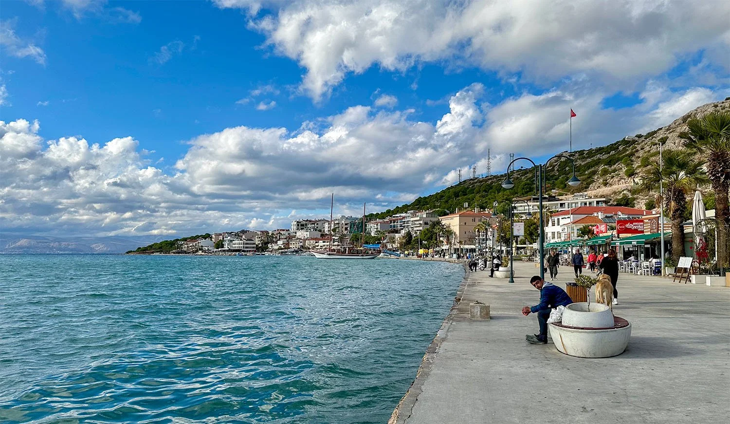 View of the waterfront at Çeşme, Türkiye, with cafes lining a wide concrete pedestrian boulevard