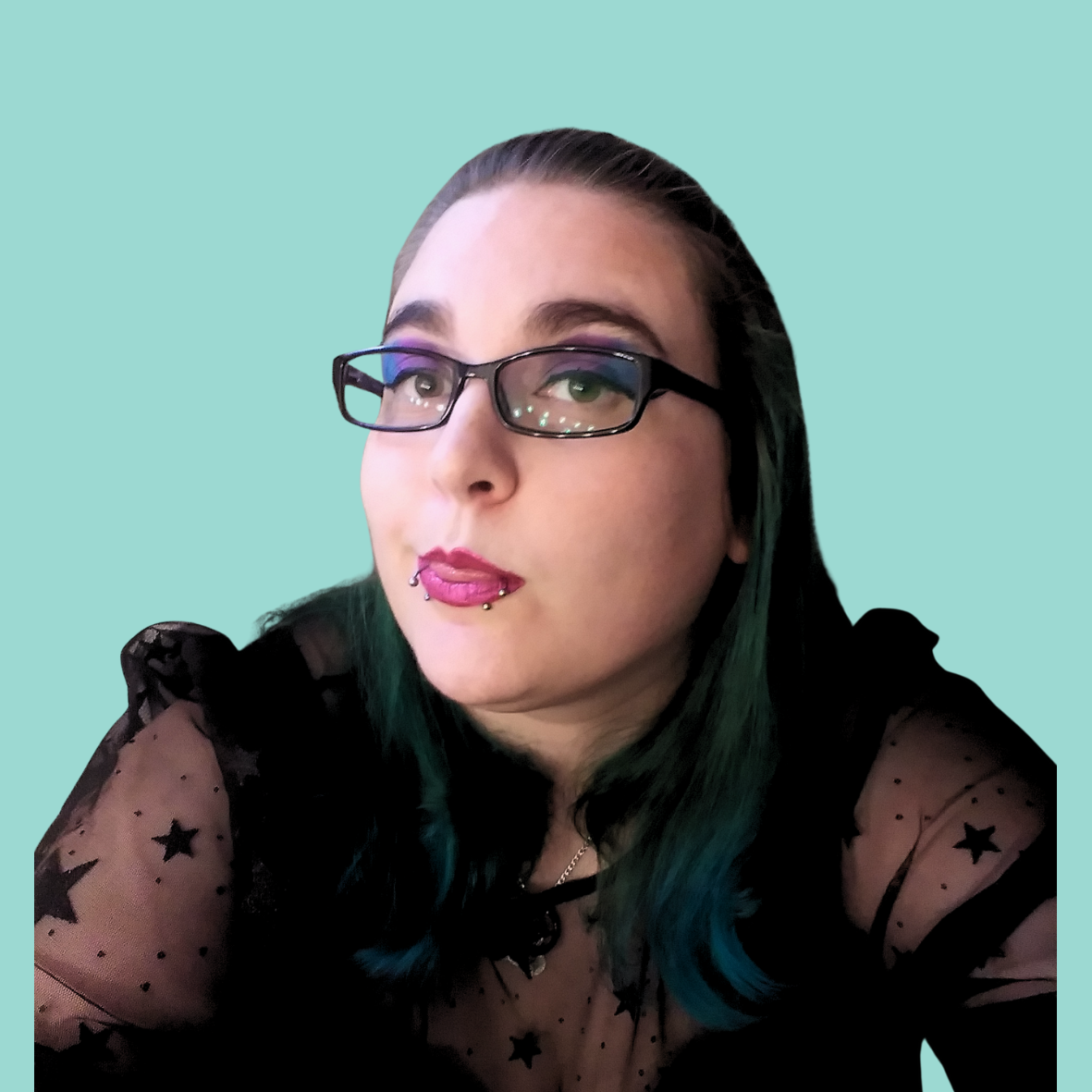 A woman with glasses and dark hair with teal tips, wearing a black sheer top with star patterns, holding a microphone, against a light teal circular background.