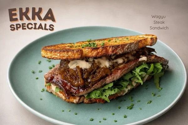Wagyu steak sandwich with grilled bread, caramelized onions, lettuce, and sauce on a blue plate