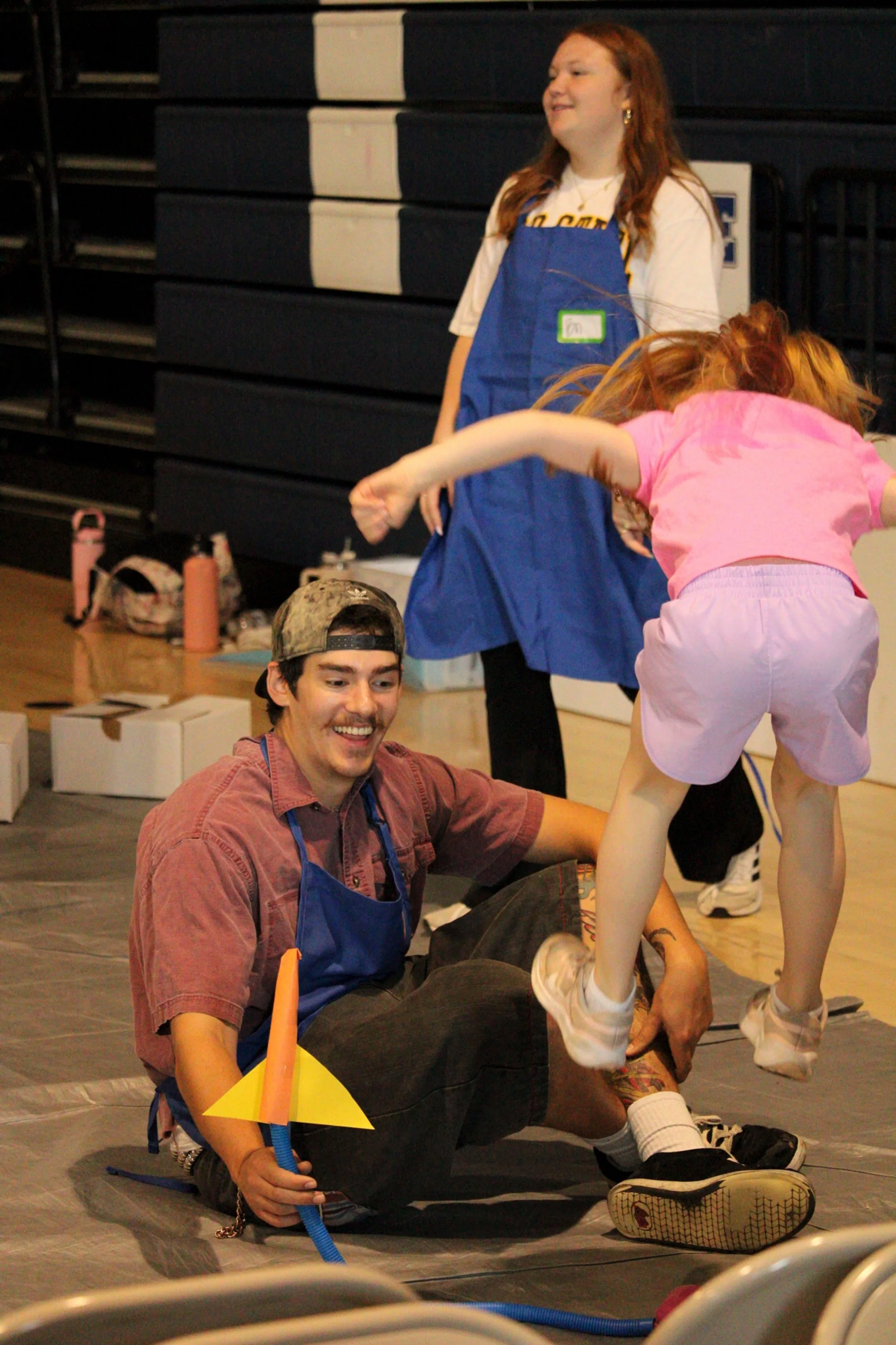 A volunteer helps a kid launch a stomp rocket while another volunteer laughs