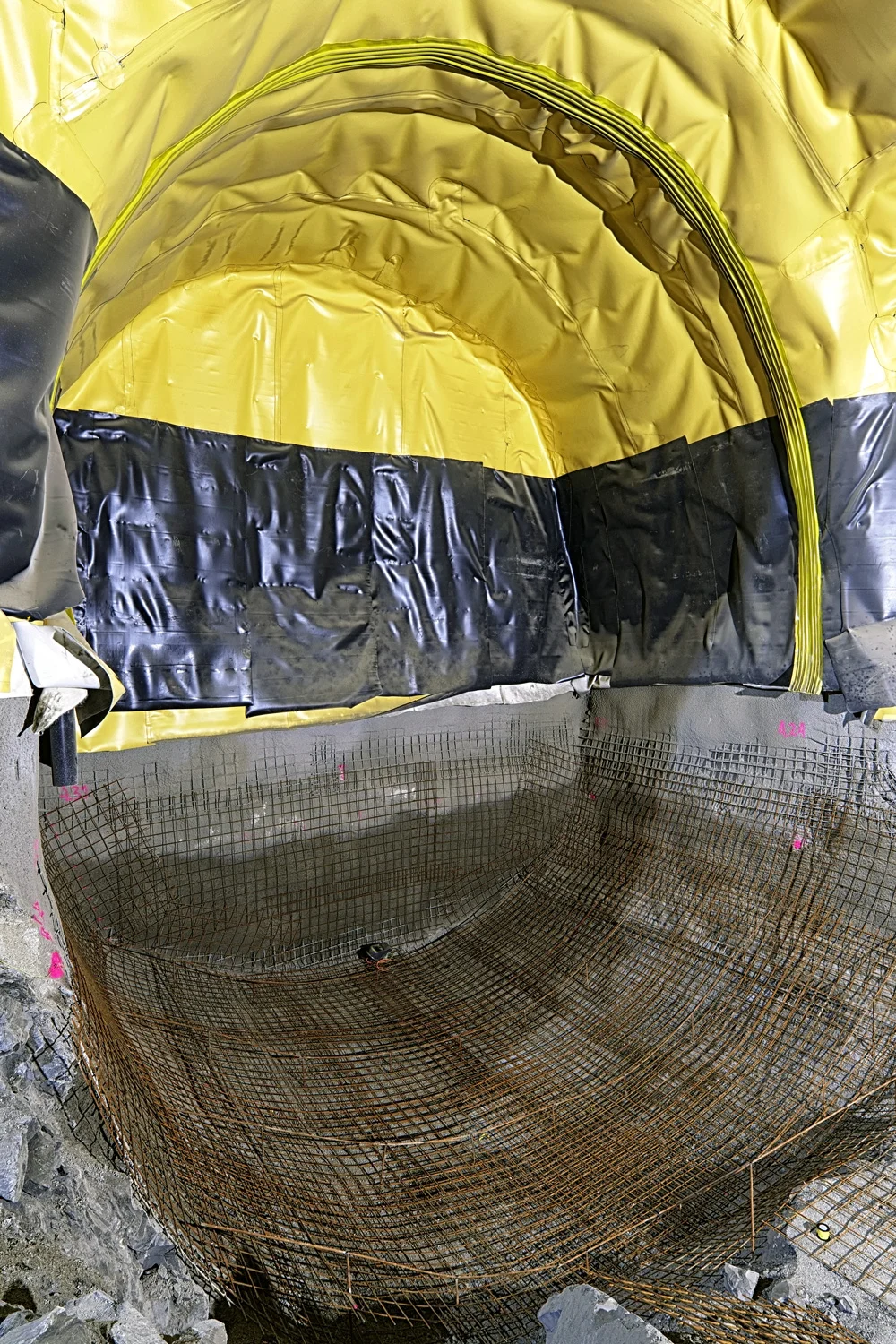 Die Zentrale Untertage im Bauzustand: In der Sohle wird die Ausbruchsicherung erstellt, bestehend aus Bewehrungsnetzen und Spritzbeton. Im Gewölbe ist die Abdichtung bereits auf der fertigen Ausbruchsicherung befestigt. In diesem Tunnelabschnitt wird später einmal der Mobilfunkraum und der Treppenabgang zum Werkleitungskanal. untergebracht.