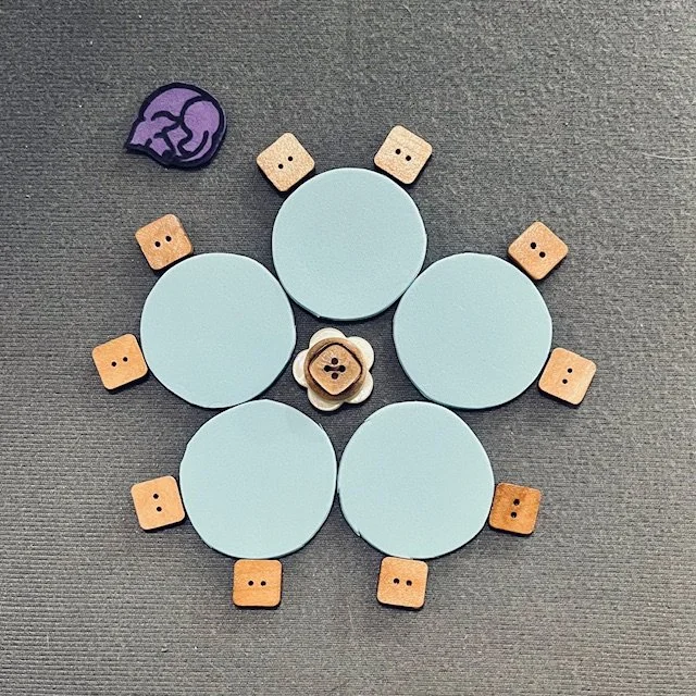 Blue circles represent small round tables. They are configured in the shape of a flower. Chairs are placed along the outer edge. An icon of a rolling chair is at the center of the flower shape. An icon of a guide dog is off to the side.