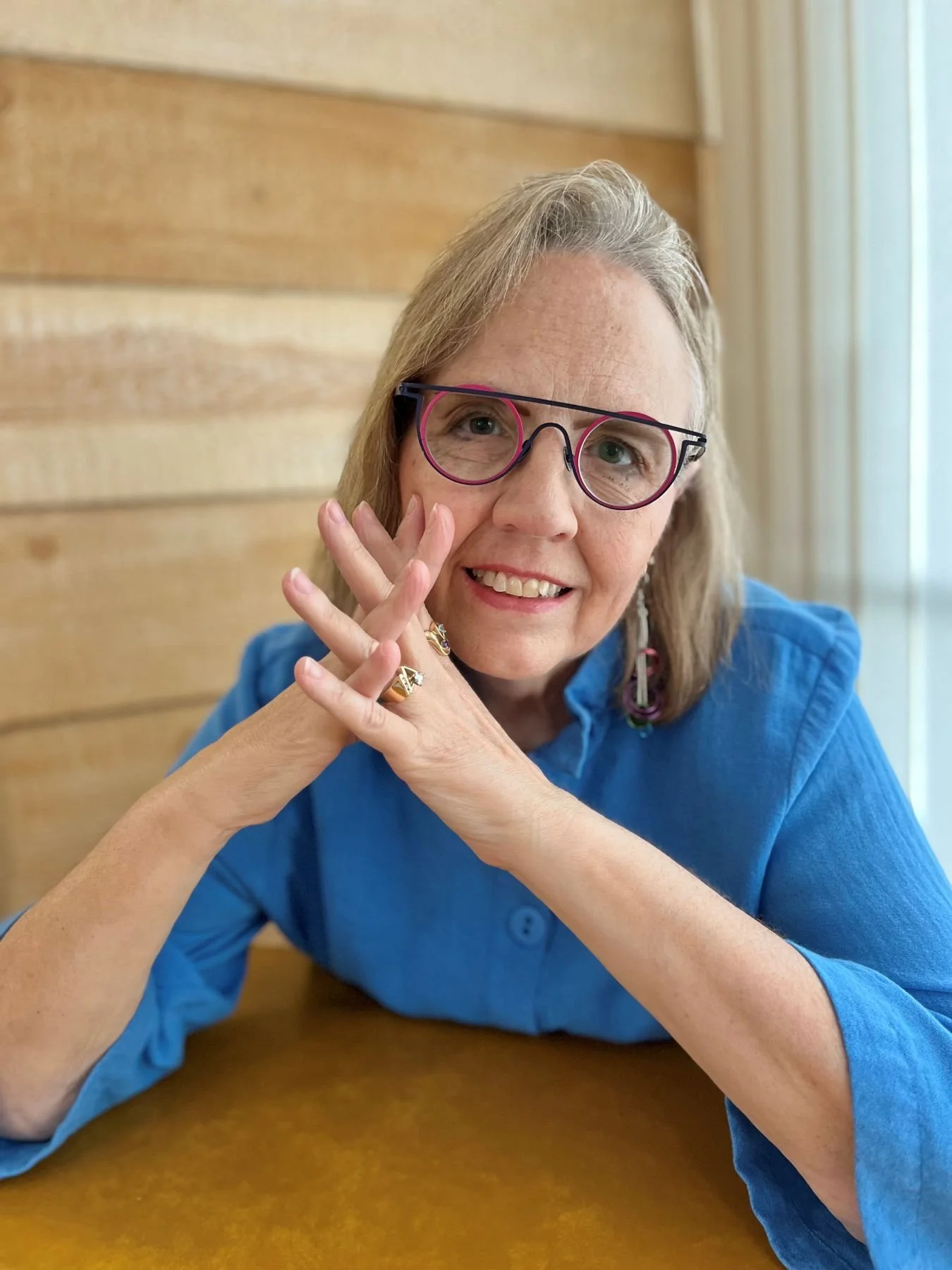 Linda Brant-Malm, an artist with blonde hair and dark rimmed glasses smiling at the camera.