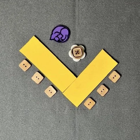 Yellow rectangles represent tables. They are configured in the shape of an L. Chairs are placed on the outer edges of the tables. Icons representing a rolling chair and a guide dog are in the crook of the L.