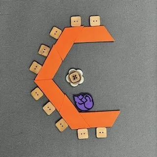 Orange trapezoid shapes represent tables. They are configured in the shape of a C. Chairs are placed along the outer edge. Icons represent a rolling chair and a guide dog in the crook of the C.