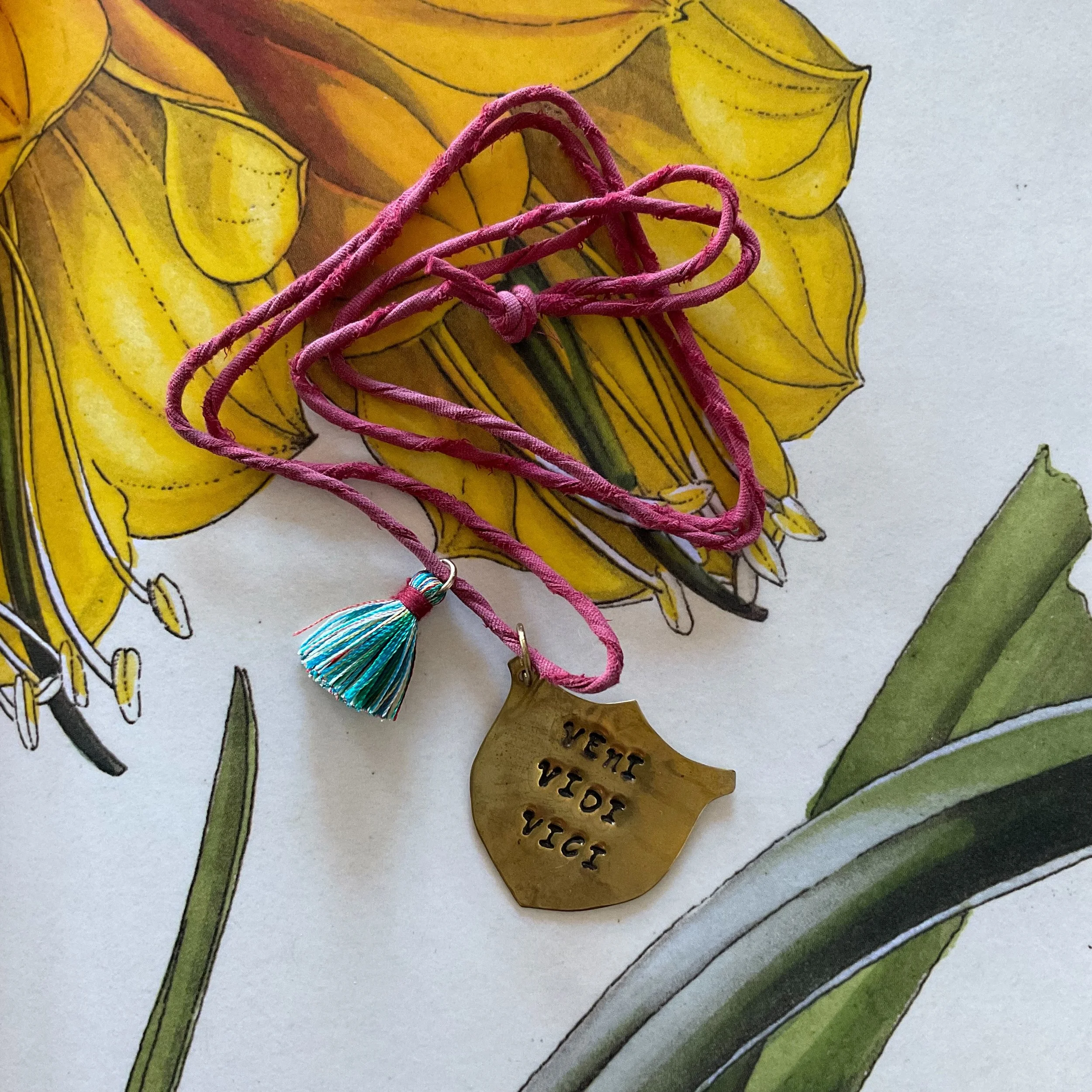 little hand-beaten shields with hopeful, insightful &amp; sometimes mouthy slogans to wear on days you need a little extra protection or a rallying cry! Sarah has suspended these on hand-twined silk cord with a joyous &amp; tactile silk tassel. In-st