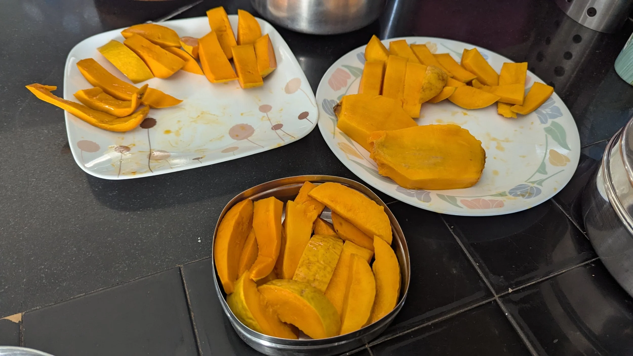 Various sliced butternut squash on multiple plates on a black countertop in a kitchen setting.
