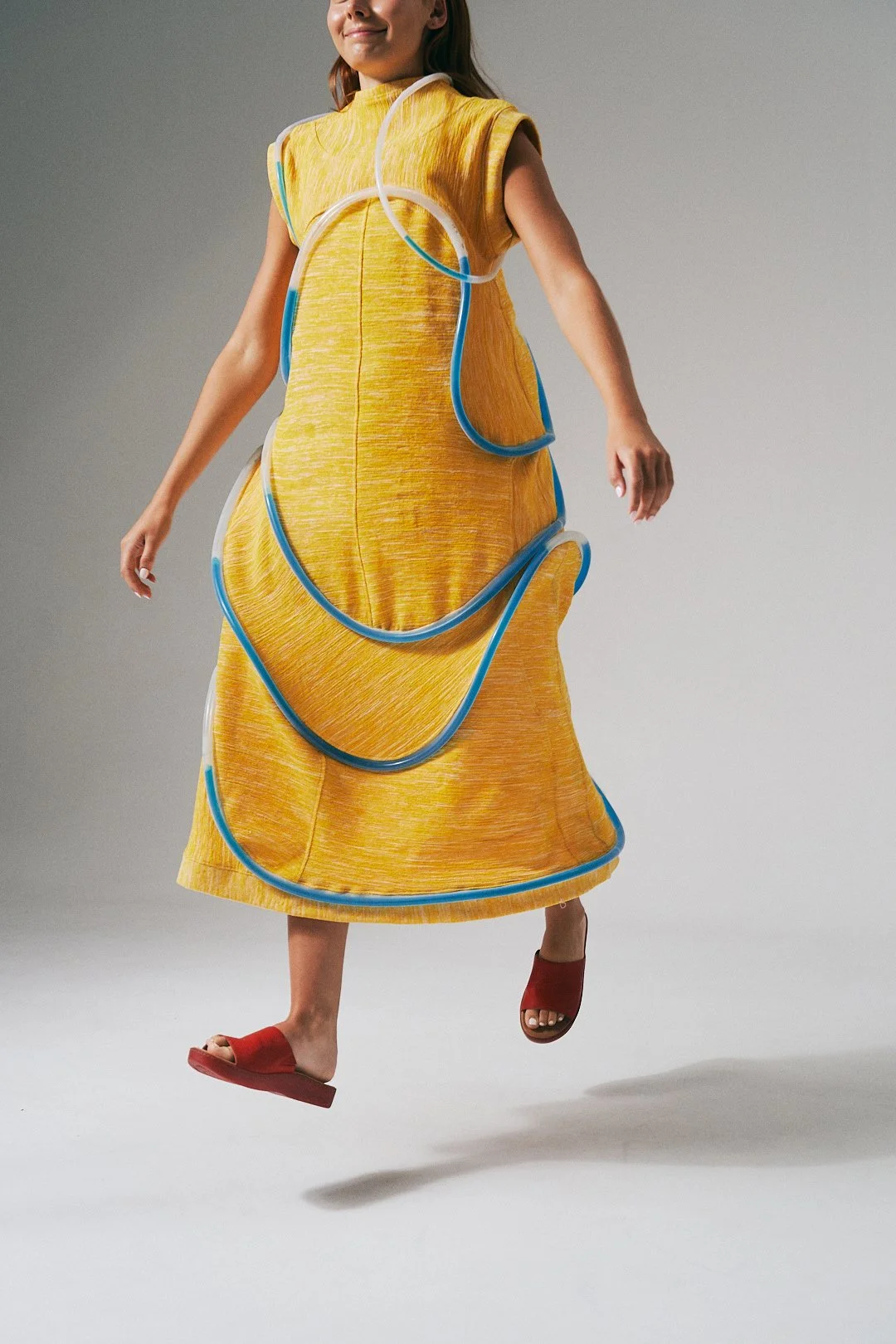 Fashion model wearing a yellow dress with blue and white tube-like accents.
