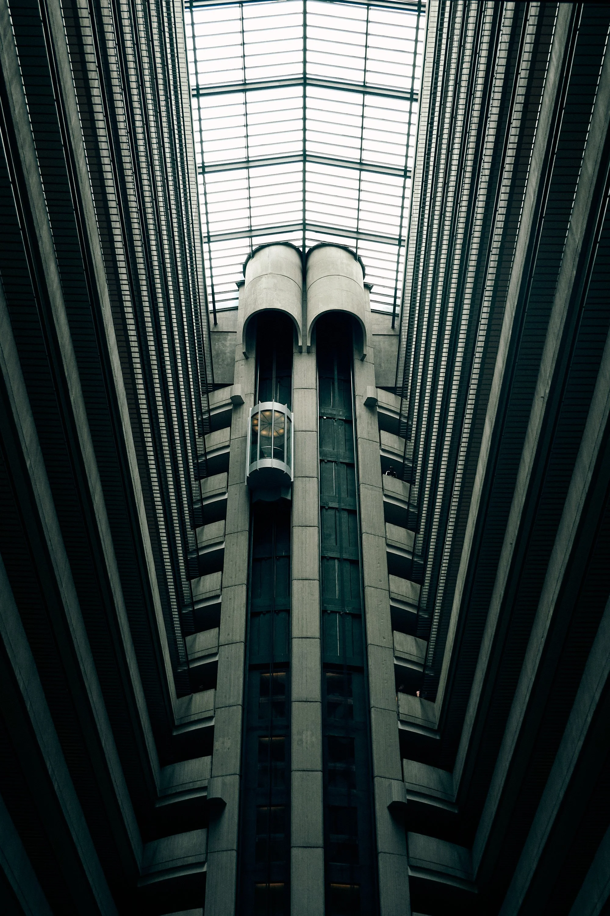 Interior view of a modern building with a central elevator shaft and a glass ceiling allowing natural light.