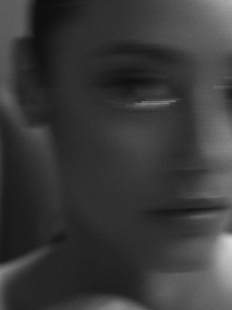 Close-up black and white photo of a person's face with glasses, partially blurred.