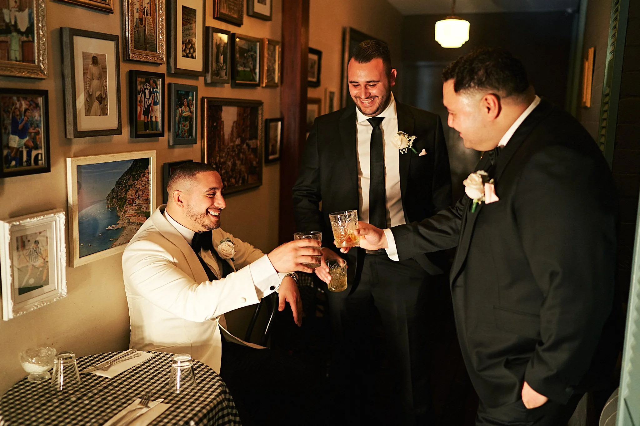 Four men in suits toasting drinks at a celebration in a cozy restaurant with framed photos on the wall.