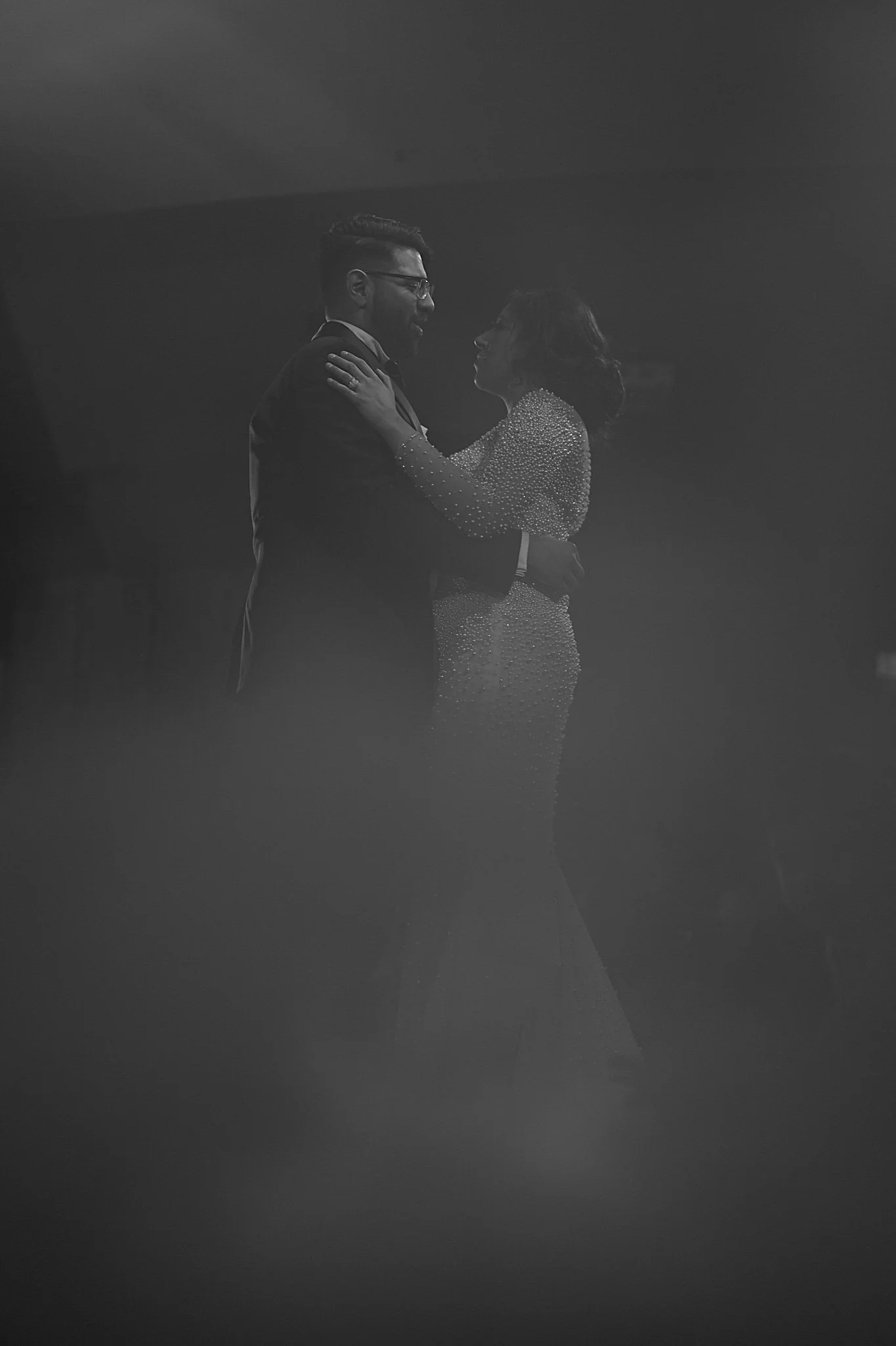 A couple dancing together, dressed in formal attire, in a dimly lit setting.