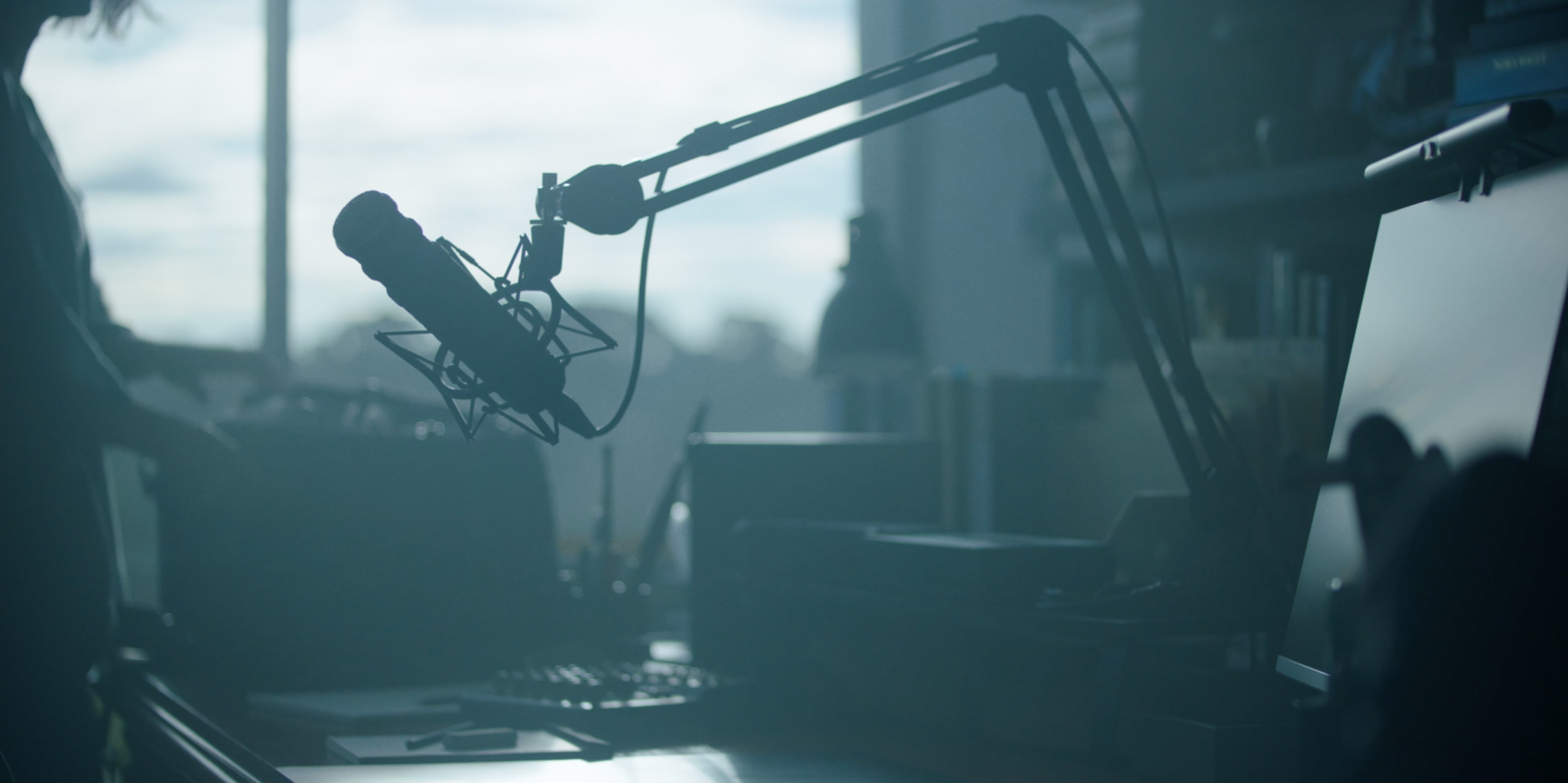 "The podcast microphone on its boom arm silhouetted against the window — a recurring visual anchor in the single-location film Monolith."