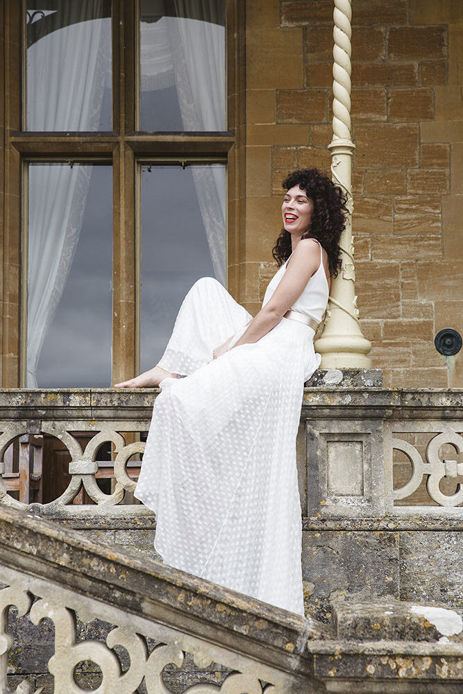 Bride casually posed on stone wall wearing Charlie Brear wedding dress. Orchardleigh Estate