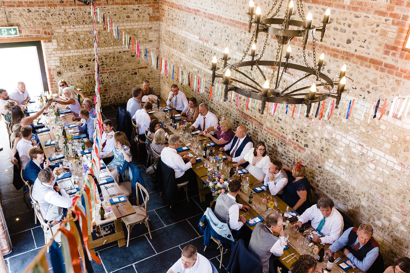 A wedding party sitting down to eat at long tables in a rustic barn