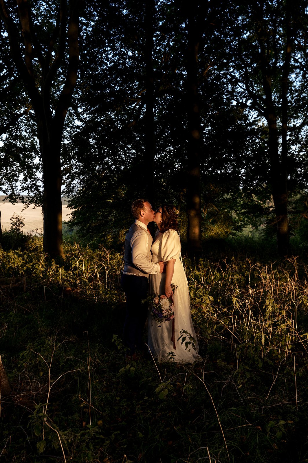 A bride and groom photographed in a woodland setting with dramatic low sunlight