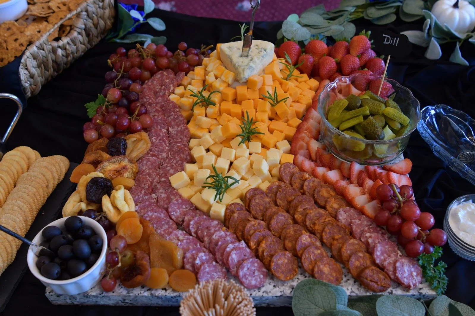 Charcuterie board with various cheeses, meats, fruits, and crackers displayed on a black tablecloth.