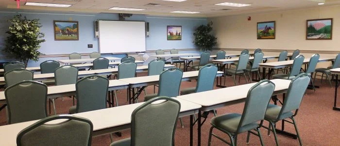 Empty conference room with rows of tables and chairs, a whiteboard at the front, and framed landscape paintings on the wall.