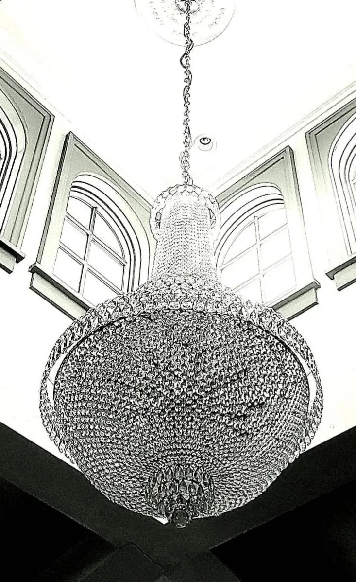 A large, ornate chandelier hanging from a white ceiling in a room with tall arched windows.