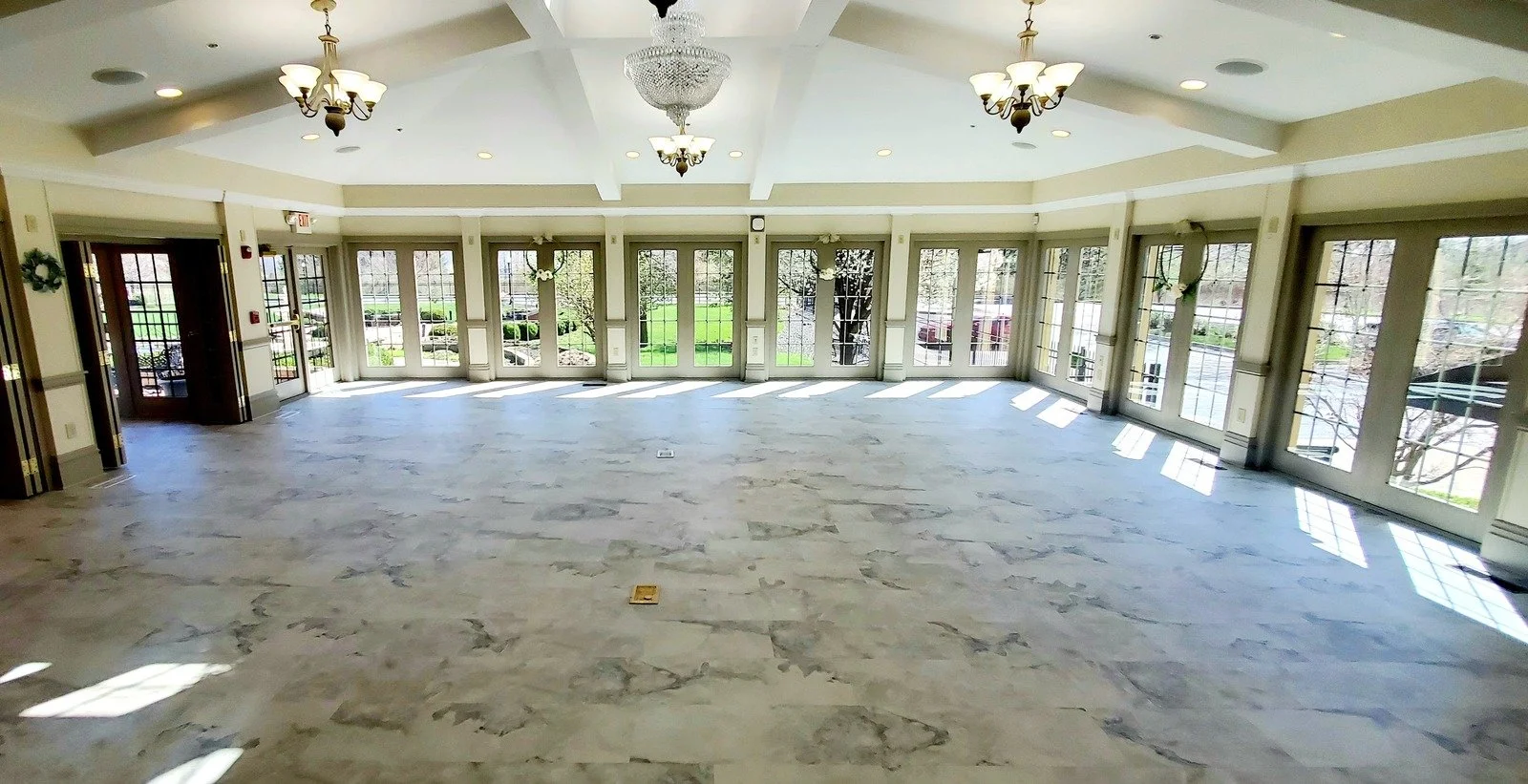 Empty banquet hall with marble flooring, large windows, and chandeliers.