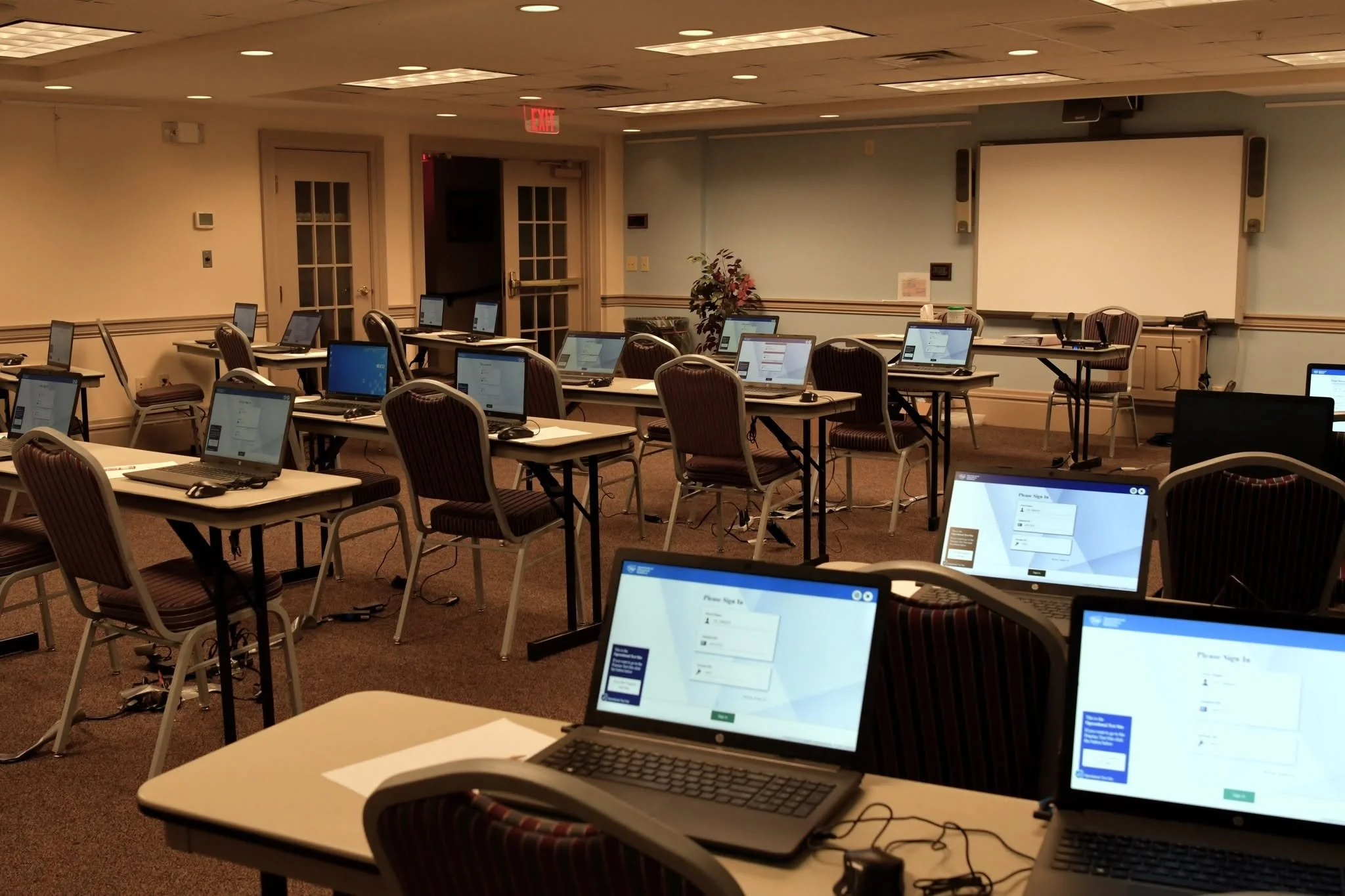 Multiple laptops set up on tables in a conference room with a whiteboard on the wall and chairs arranged for a training or meeting session.
