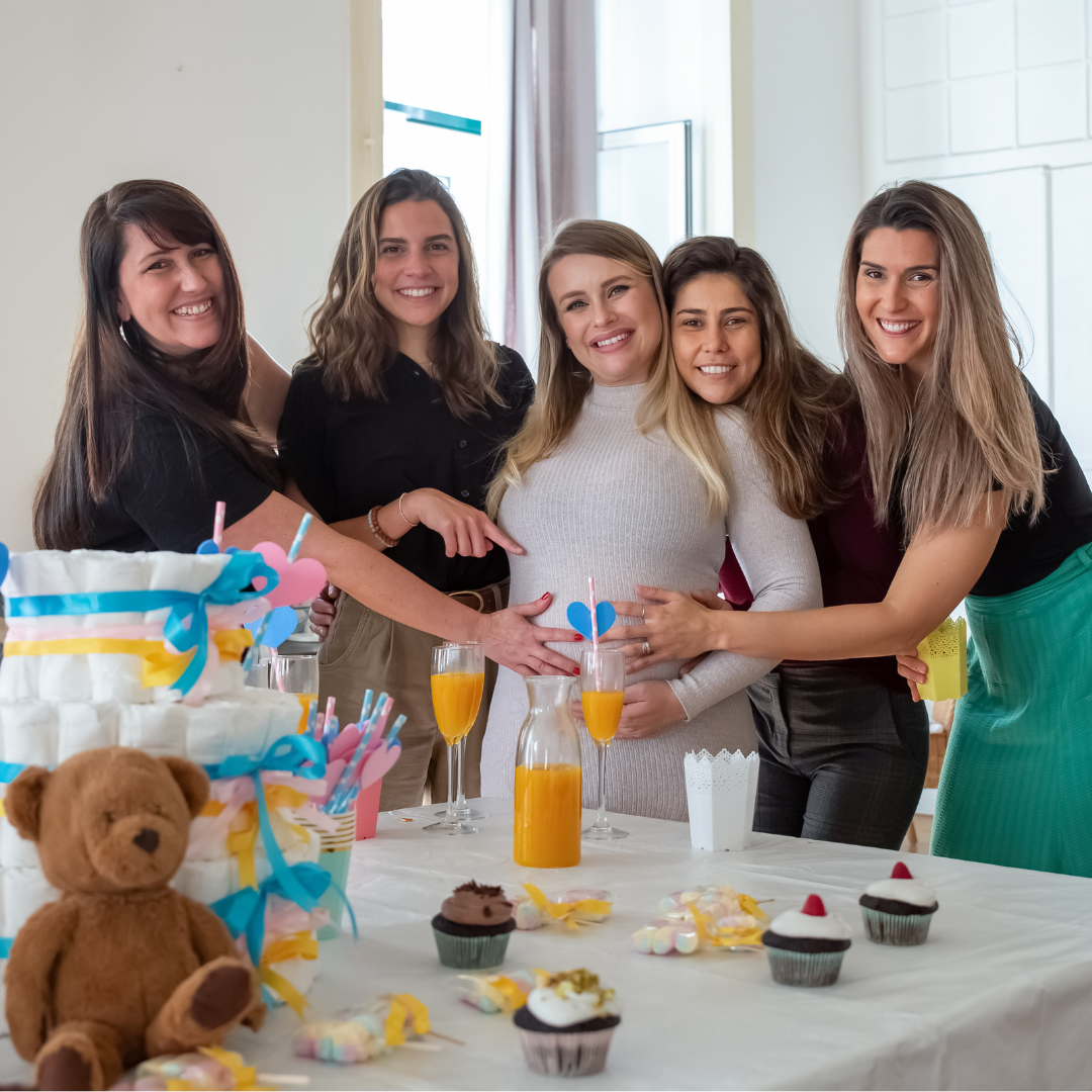 Five women smiling and hugging at a party table decorated with desserts and drinks.