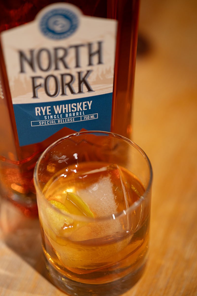 Bottle of North Fork Blue Label on a wood table next to a cocktail drink