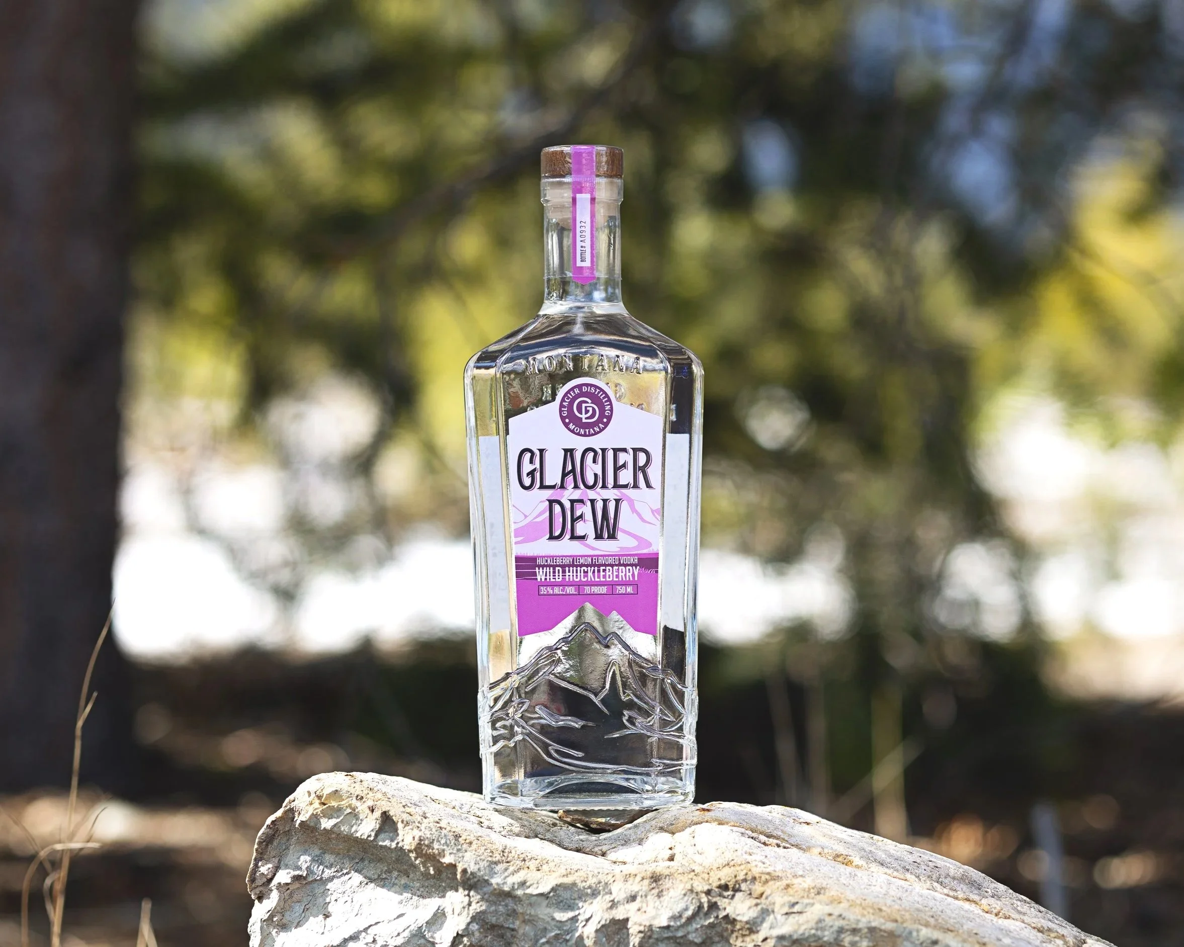 Bottle of Glacier Dew Wild Huckleberry sitting on a rock with greenery and foliage in the background.
