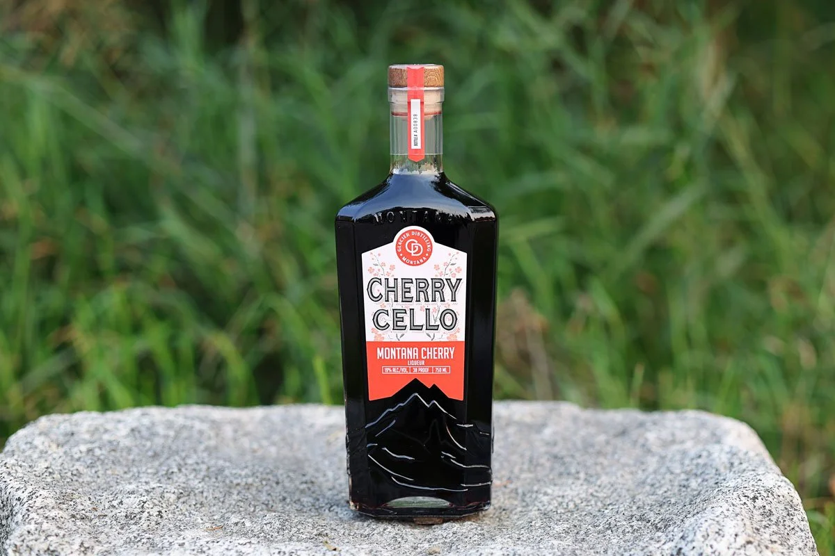 Bottle of Cherrycello sitting on a rock with fall foliage in the background.