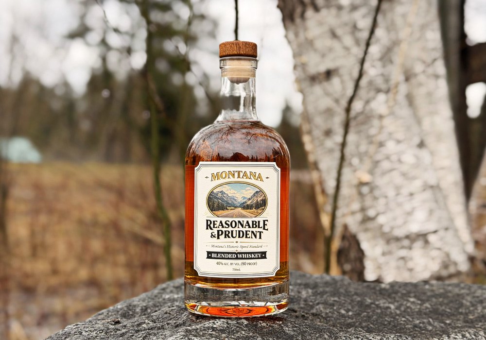 A glass bottle of Reasonable and Prudent Blended whiskey from Glacier distilling sitting on a rock with foliage in the background.