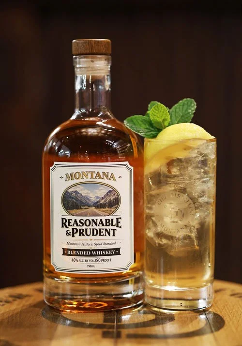 bottle of Reasonable and Prudent sitting on a stool next to a Montana Highball cocktail with a brown background.
