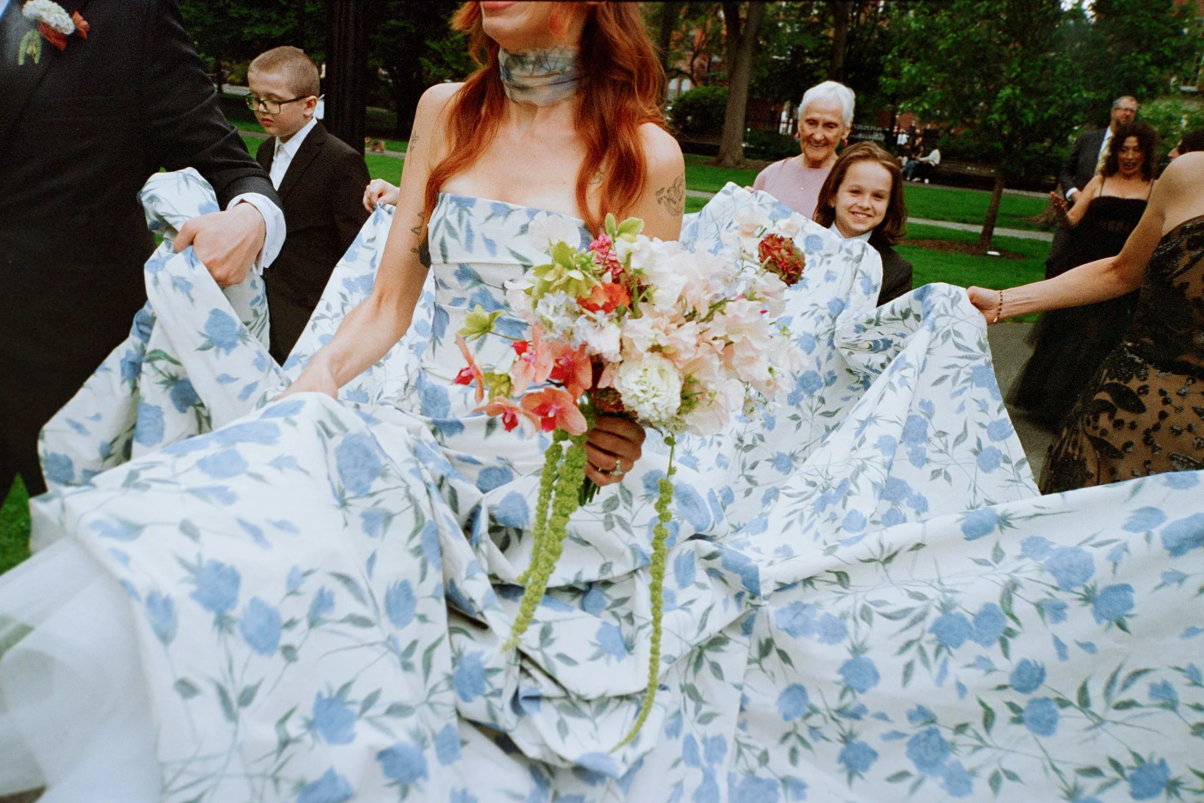A bride in a blue floral dress, with her family holding each a bit of the dress.