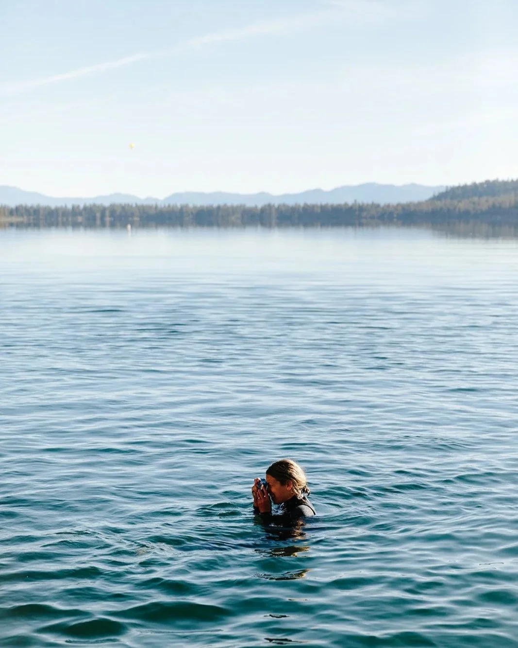 A photographer, wearing a wetsuit and treading water in Fallen Leaf Lake, California.