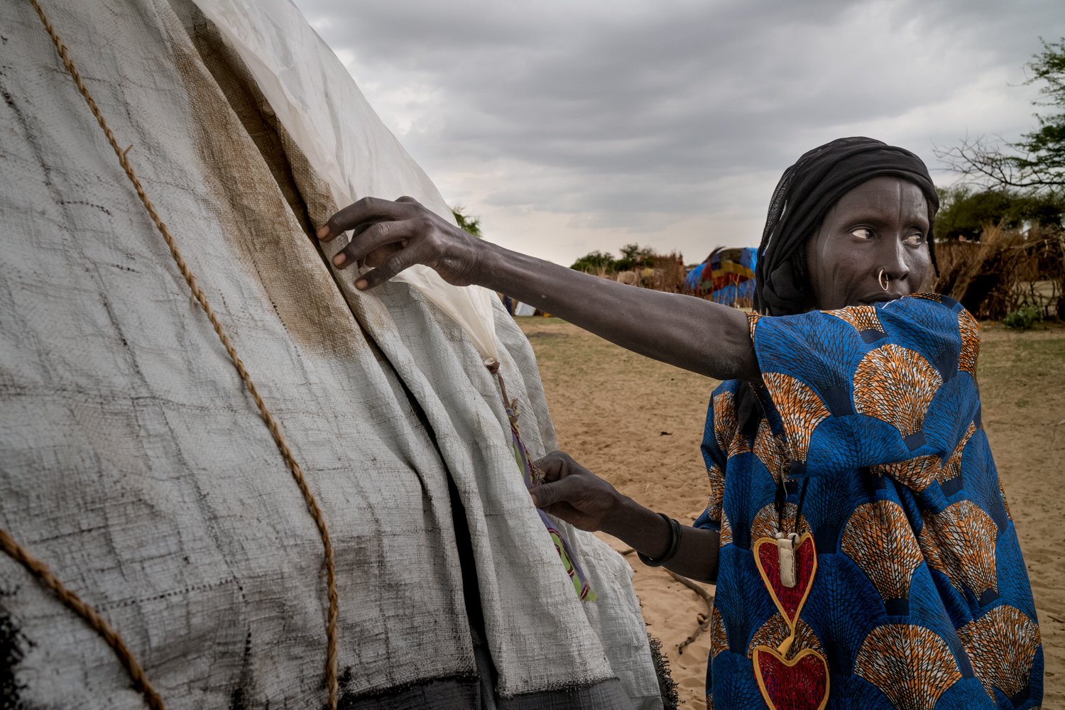  In der Regenzeit im Jahr 2021 schützt eine Frau im Tschad ihr Zelt mit einer Plastikplane vor dem aufziehenden Sturm. Aufgrund des Klimawandels sind  Niederschläge zuletzt immer unberechenbarer geworden. 