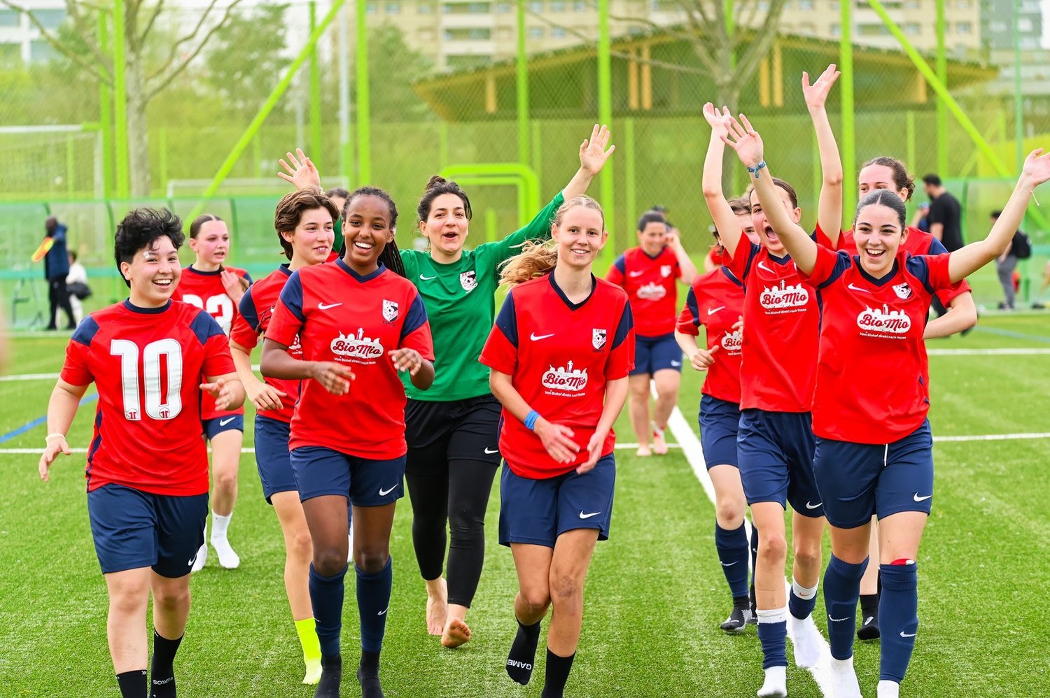 Spielerinnen in roten Trikots jubeln auf dem Kunstrasen