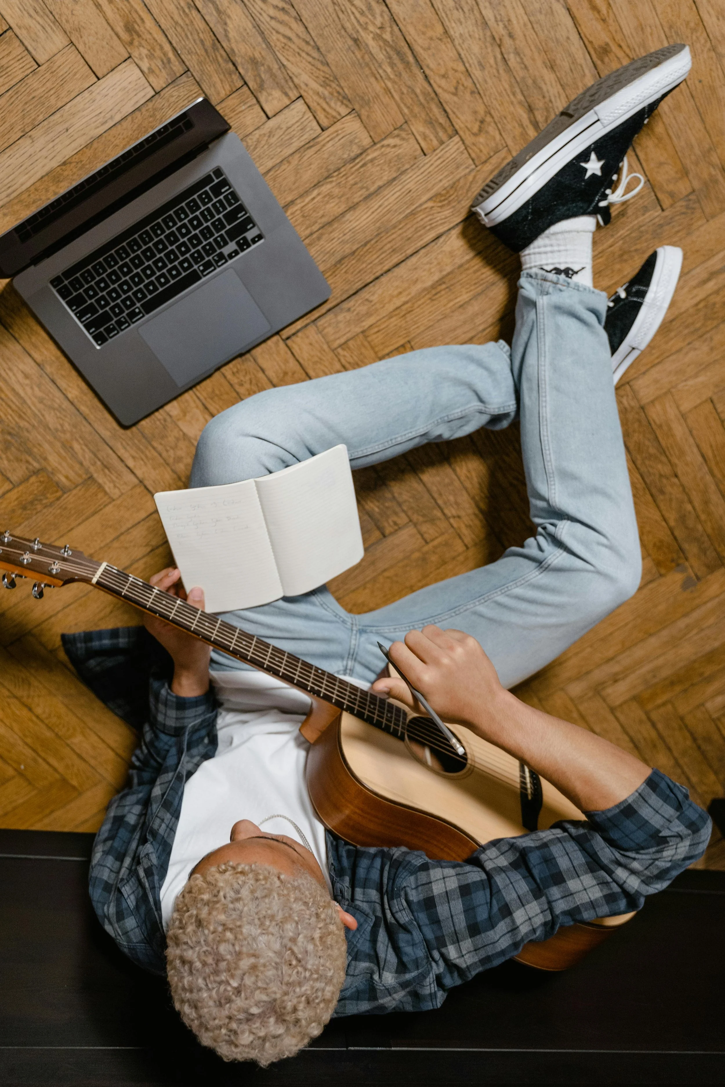 Teenage student practicing chords on guitar while following along on a laptop during a virtual guitar lesson