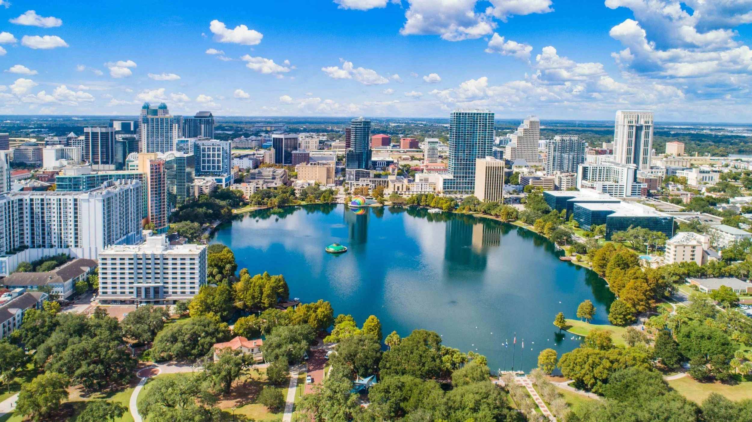 A sunny aerial shot of Orlando with a lake in the middle of an urban park amongst skyscrapers in the city center