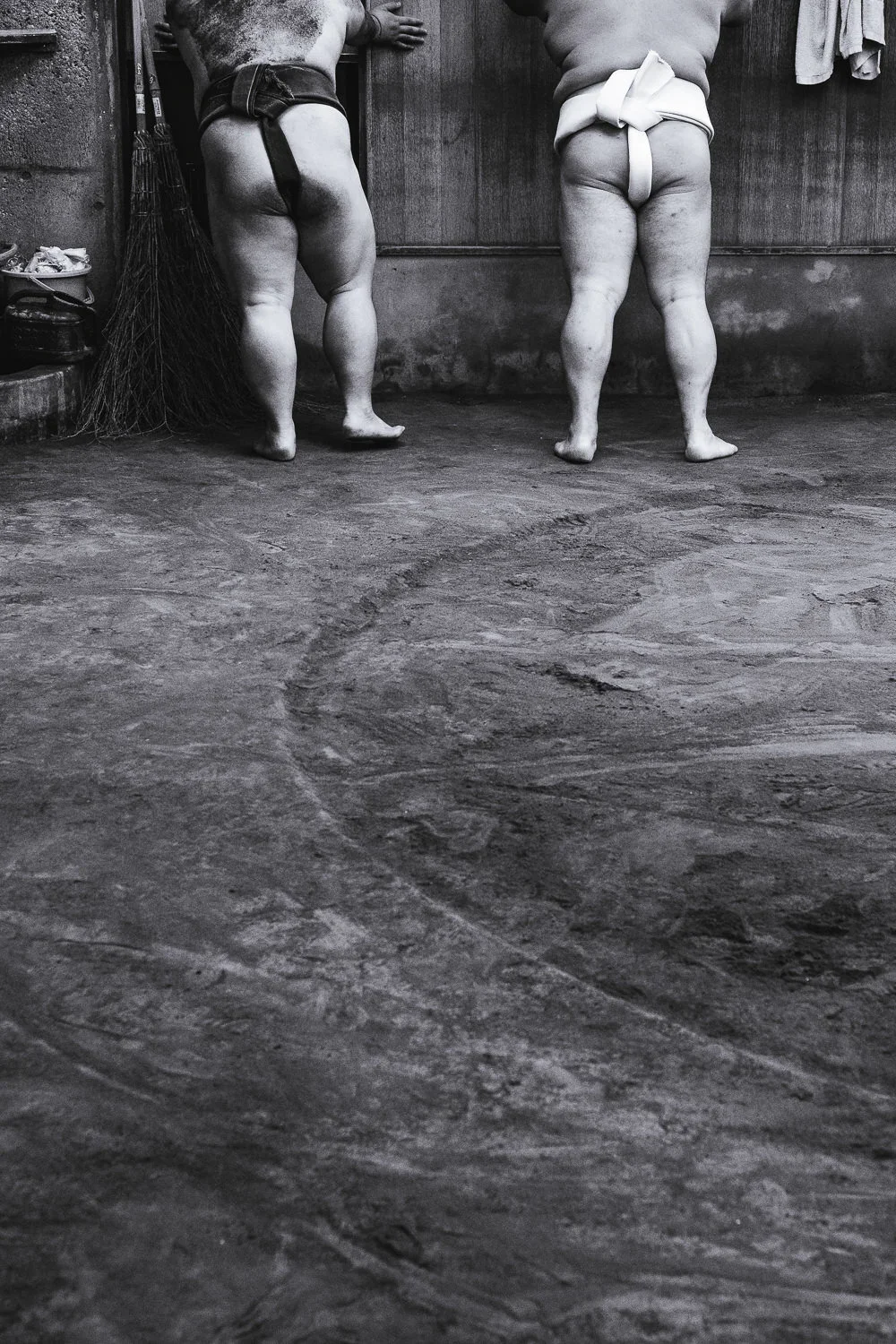 Two sumo wrestlers rest against a wall in their sumo stable in Tokyo, Japan
