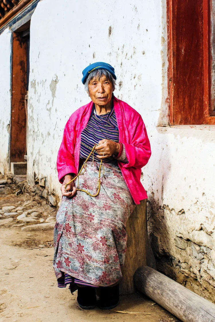 Elderly grandmother sits outside her home holding prayer beads in rural Bhutan