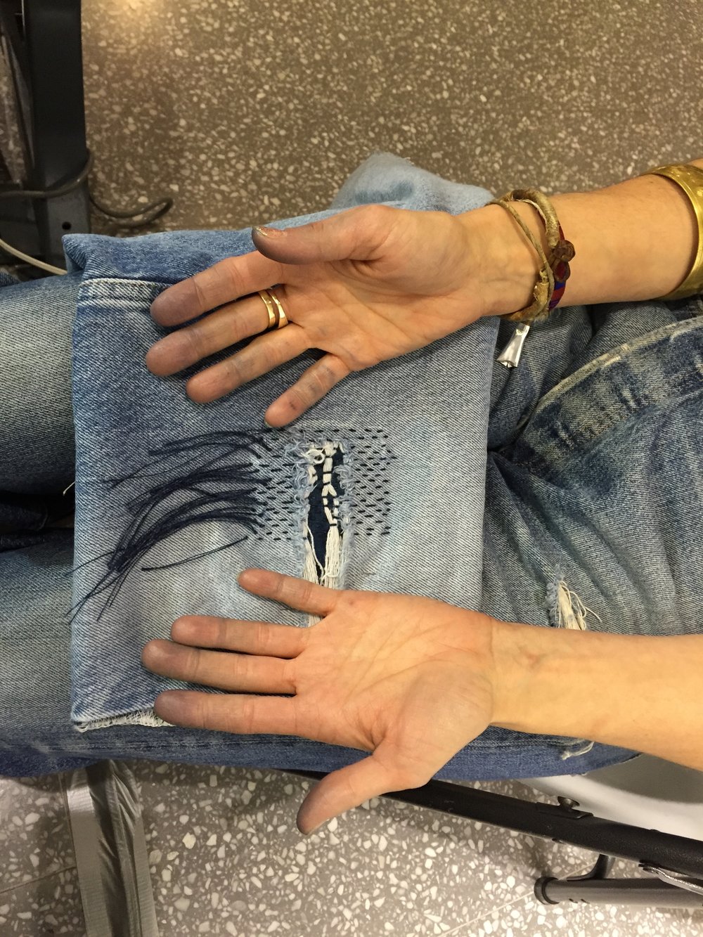 Indigo stained hands over a pair of repaired jeans. 